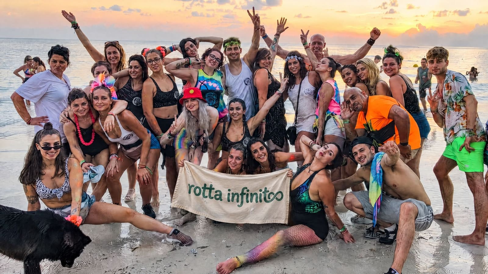 Il gruppo sulla spiaggia al tramonto con vestiti colorati e lo striscione
